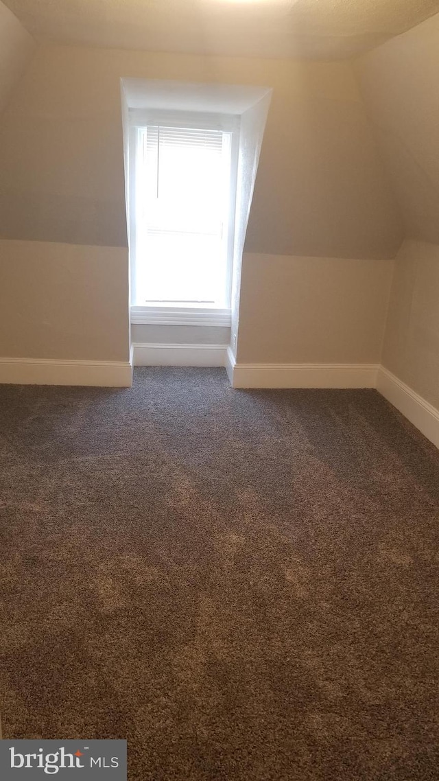 additional living space with lofted ceiling, dark carpet, and baseboards