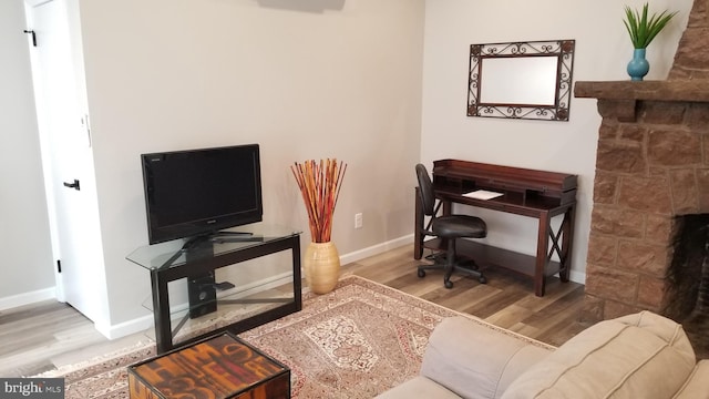 office area with a fireplace, baseboards, and wood finished floors