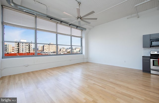 unfurnished room with light wood-style floors, a view of city, ceiling fan, and baseboards