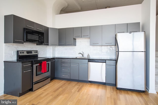 kitchen with stainless steel appliances, dark countertops, decorative backsplash, light wood-style floors, and a sink