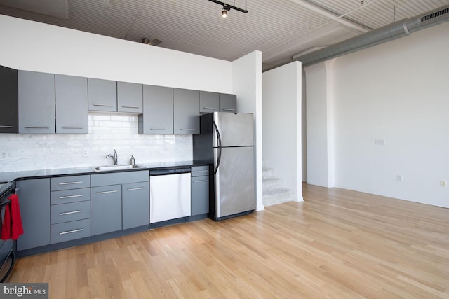 kitchen with tasteful backsplash, gray cabinets, stainless steel appliances, light wood-type flooring, and a sink