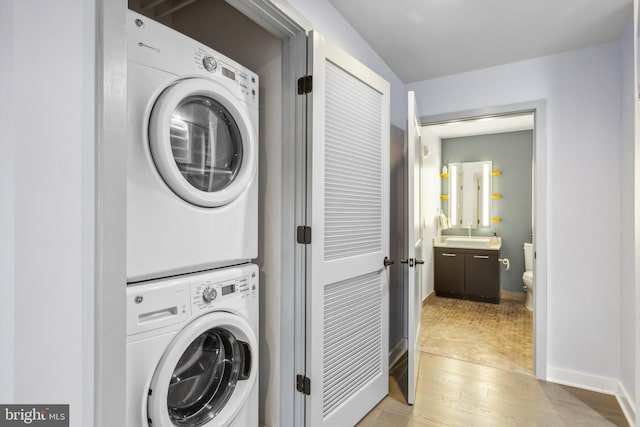 washroom featuring laundry area, baseboards, light wood-style floors, and stacked washer / drying machine