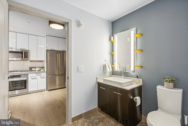 bathroom with toilet, decorative backsplash, vanity, wood finished floors, and baseboards