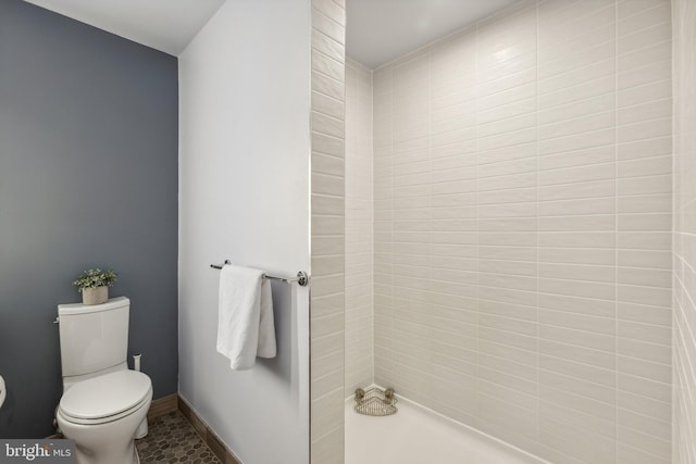 bathroom with tiled shower, toilet, and baseboards