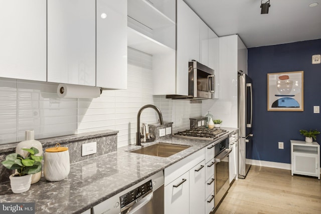 kitchen with a sink, white cabinets, appliances with stainless steel finishes, decorative backsplash, and dark stone counters