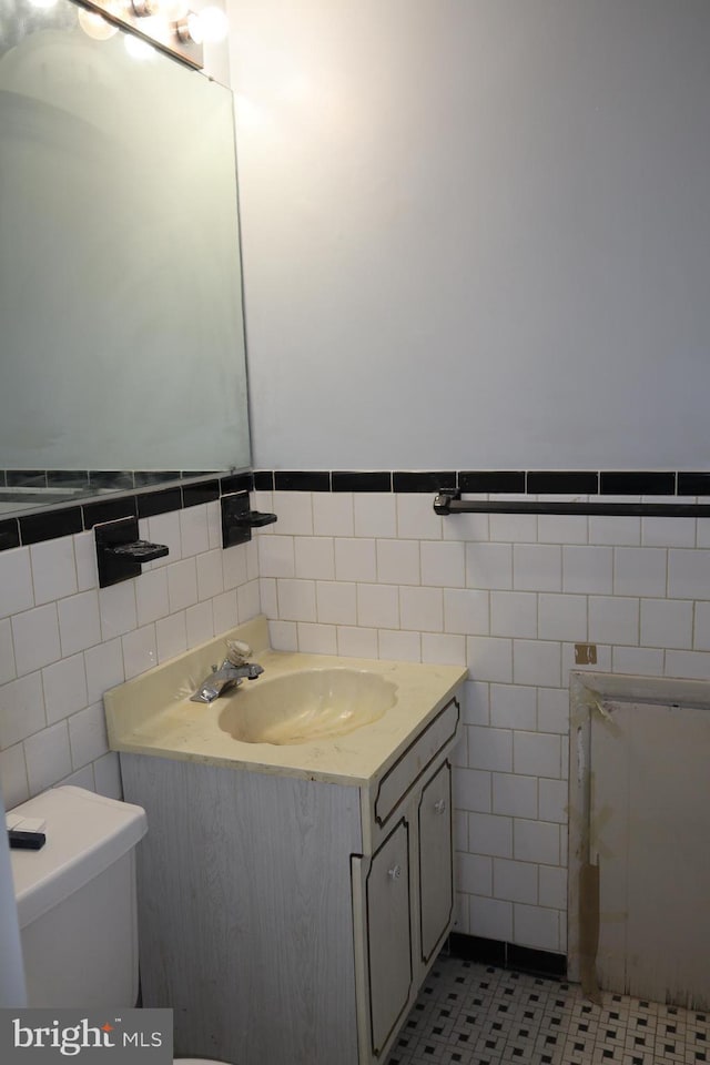 half bath with tile walls, vanity, toilet, and tile patterned floors