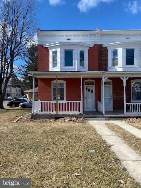 view of front of home with covered porch, brick siding, and a front lawn