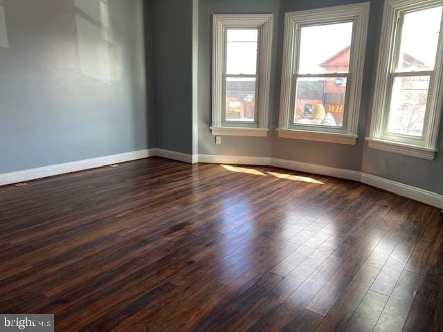 spare room featuring baseboards, dark wood-type flooring, and a wealth of natural light