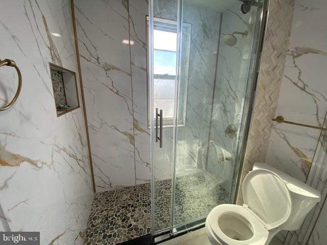 bathroom with toilet, stone wall, a marble finish shower, and a healthy amount of sunlight