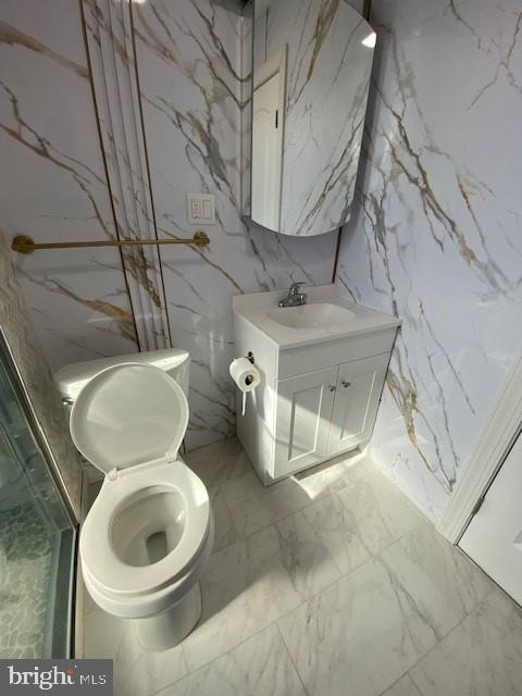 bathroom featuring toilet, stone wall, vanity, and marble finish floor