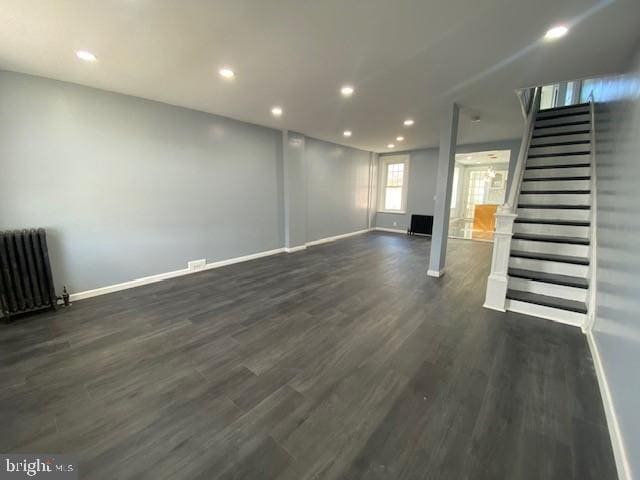 unfurnished living room with baseboards, radiator heating unit, dark wood-type flooring, stairs, and recessed lighting