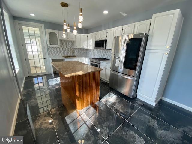 kitchen with a center island, hanging light fixtures, backsplash, appliances with stainless steel finishes, and white cabinetry