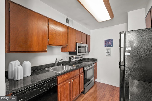 kitchen featuring visible vents, brown cabinetry, light wood-style flooring, black appliances, and a sink