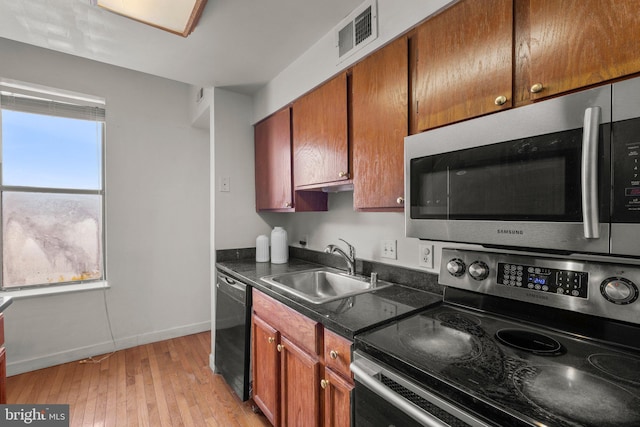 kitchen with a sink, visible vents, appliances with stainless steel finishes, brown cabinetry, and dark countertops