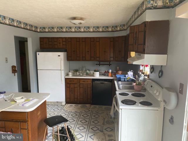 kitchen with white appliances, light countertops, a textured ceiling, under cabinet range hood, and a sink