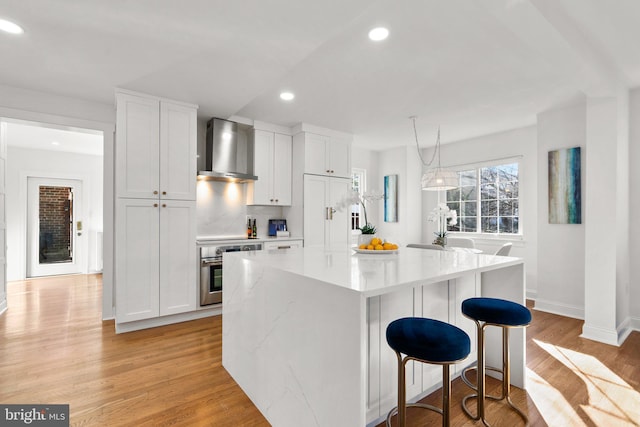 kitchen featuring recessed lighting, light wood-style flooring, a kitchen island, wall chimney range hood, and oven