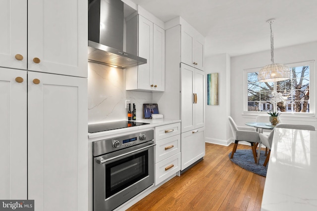 kitchen with light wood-style flooring, white cabinets, oven, wall chimney exhaust hood, and black electric cooktop