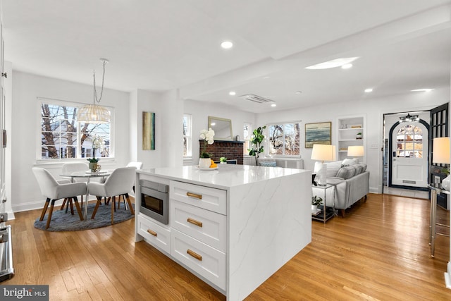 kitchen featuring built in shelves, white cabinets, light stone countertops, light wood finished floors, and stainless steel microwave