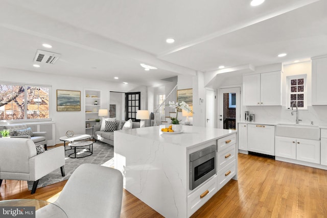 kitchen with light wood finished floors, stainless steel microwave, paneled dishwasher, open floor plan, and a sink