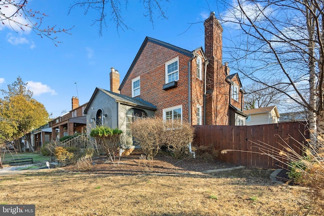 view of side of property with a yard, brick siding, fence, and a chimney