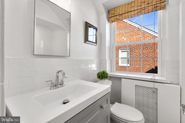 bathroom featuring toilet, vanity, tile walls, wainscoting, and radiator