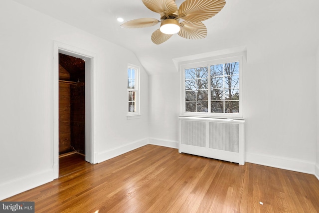 unfurnished bedroom featuring light wood-type flooring, a walk in closet, baseboards, and radiator heating unit