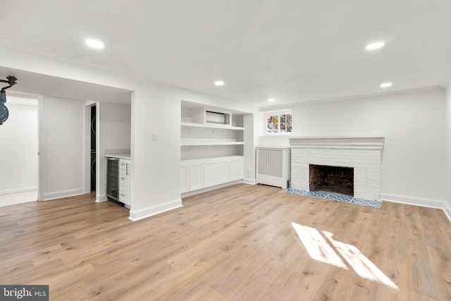 unfurnished living room featuring built in features, wine cooler, recessed lighting, light wood-style floors, and a brick fireplace