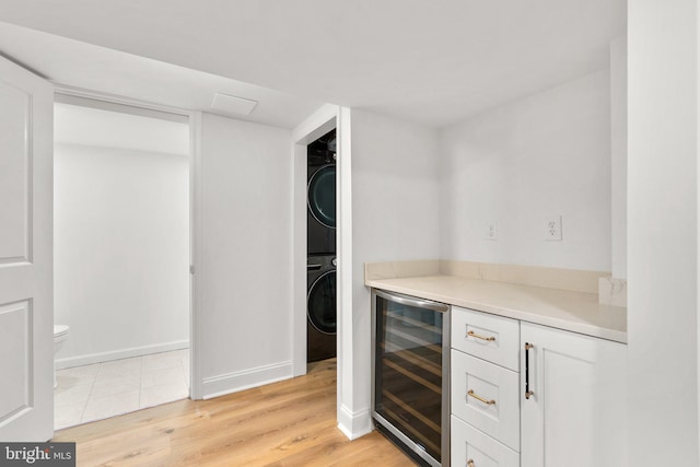 bar with wine cooler, stacked washer and clothes dryer, a dry bar, light wood-style flooring, and baseboards