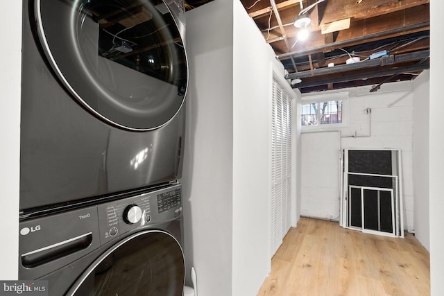 clothes washing area featuring laundry area, stacked washing maching and dryer, and wood finished floors