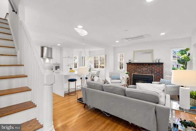 living area with recessed lighting, visible vents, light wood-style floors, stairway, and a brick fireplace