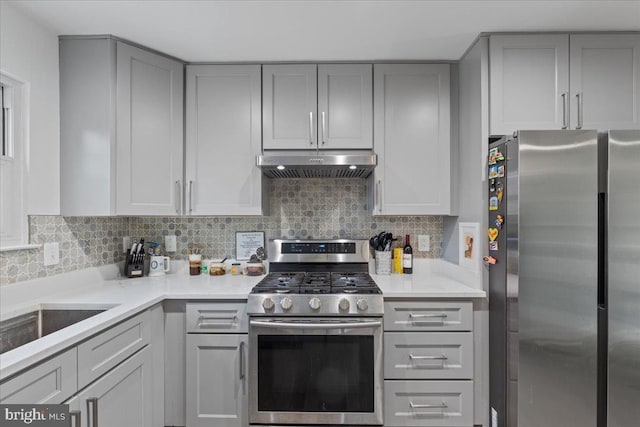 kitchen featuring under cabinet range hood, light countertops, appliances with stainless steel finishes, backsplash, and gray cabinets