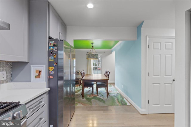 kitchen featuring hanging light fixtures, decorative backsplash, freestanding refrigerator, light wood-type flooring, and baseboards