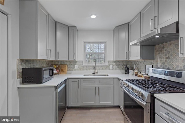 kitchen with under cabinet range hood, stainless steel appliances, a sink, light countertops, and gray cabinets