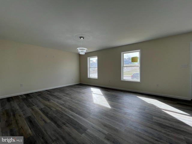 empty room with an inviting chandelier, baseboards, and dark wood-style flooring