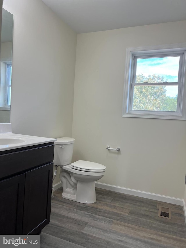 half bathroom featuring visible vents, toilet, vanity, wood finished floors, and baseboards