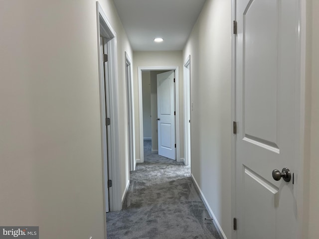 corridor featuring baseboards and dark colored carpet