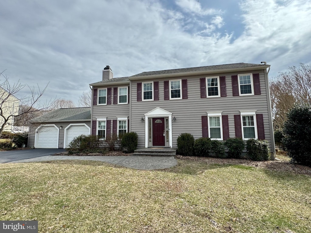 colonial home with a garage, a chimney, a front lawn, and aphalt driveway