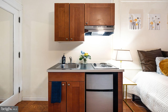 kitchen featuring under cabinet range hood, a sink, freestanding refrigerator, white electric stovetop, and brown cabinetry