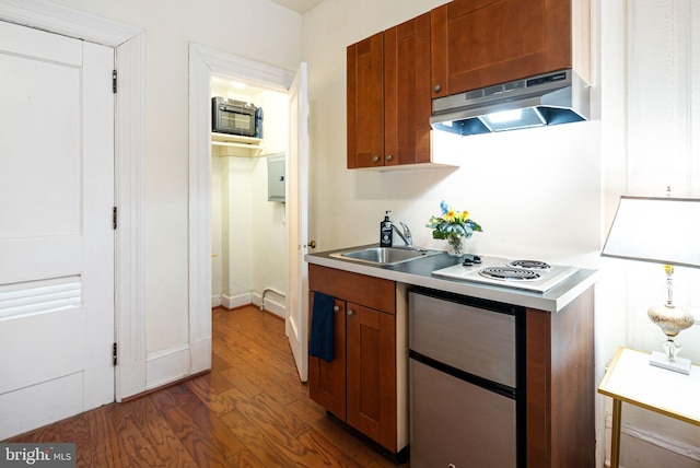 kitchen featuring brown cabinets, dark wood-type flooring, light countertops, under cabinet range hood, and a sink