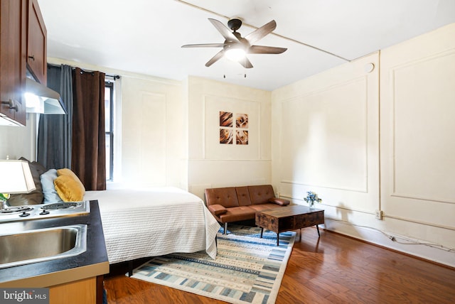 bedroom featuring dark wood-type flooring, a sink, a decorative wall, and a ceiling fan