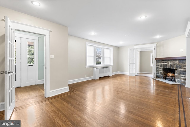 unfurnished living room with radiator, a healthy amount of sunlight, a fireplace, and wood finished floors