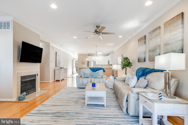 living room featuring ornamental molding, a fireplace, visible vents, and light wood-style floors