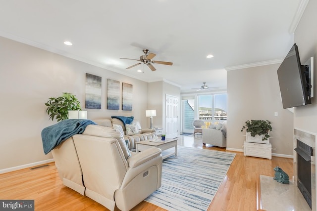 living room with a fireplace with flush hearth, baseboards, light wood-style flooring, and crown molding