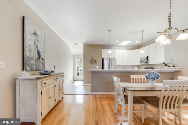 dining space with baseboards, ornamental molding, a skylight, and light wood-style floors