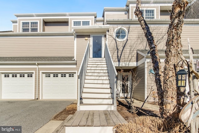 multi unit property with aphalt driveway, stairway, and an attached garage