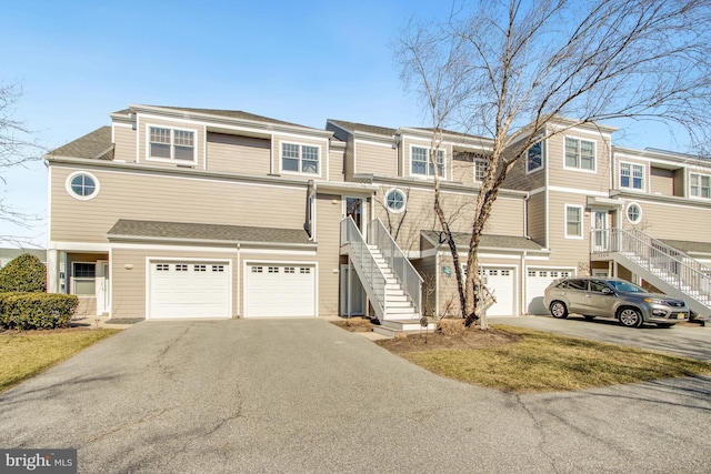 multi unit property featuring a garage, driveway, stairway, and roof with shingles