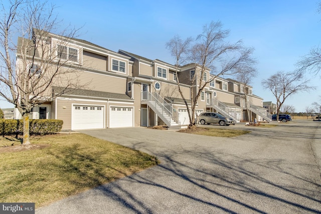 view of property featuring a garage, stairs, a residential view, and aphalt driveway