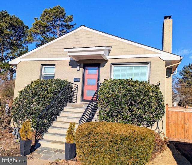 bungalow with a chimney, fence, and brick siding