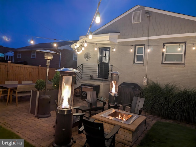 rear view of house with brick siding, fence, a fire pit, and a patio