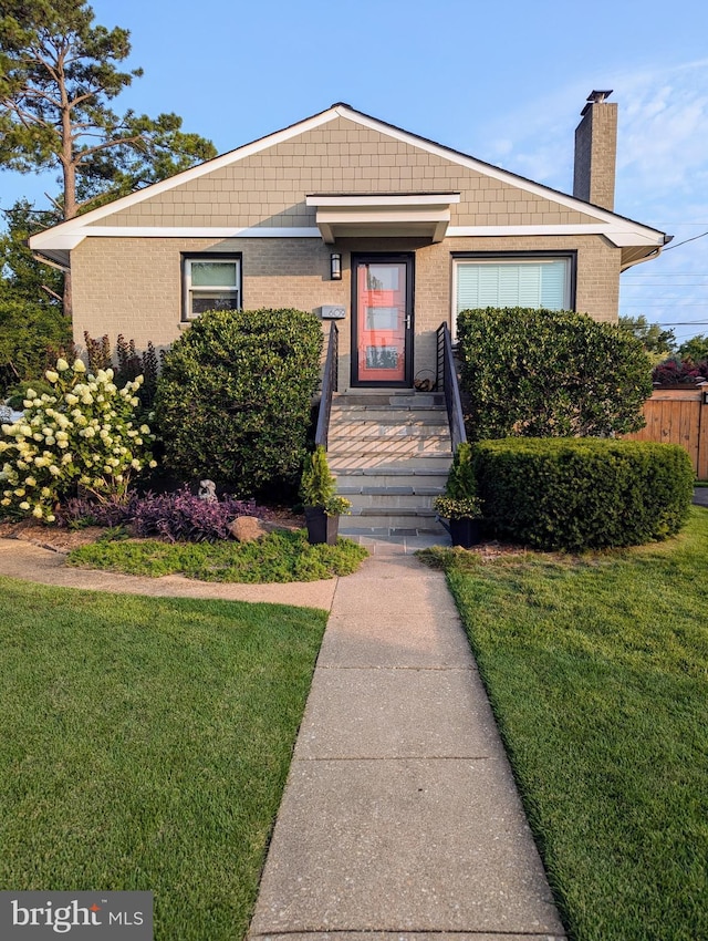 bungalow-style house featuring brick siding, a front lawn, a chimney, and fence